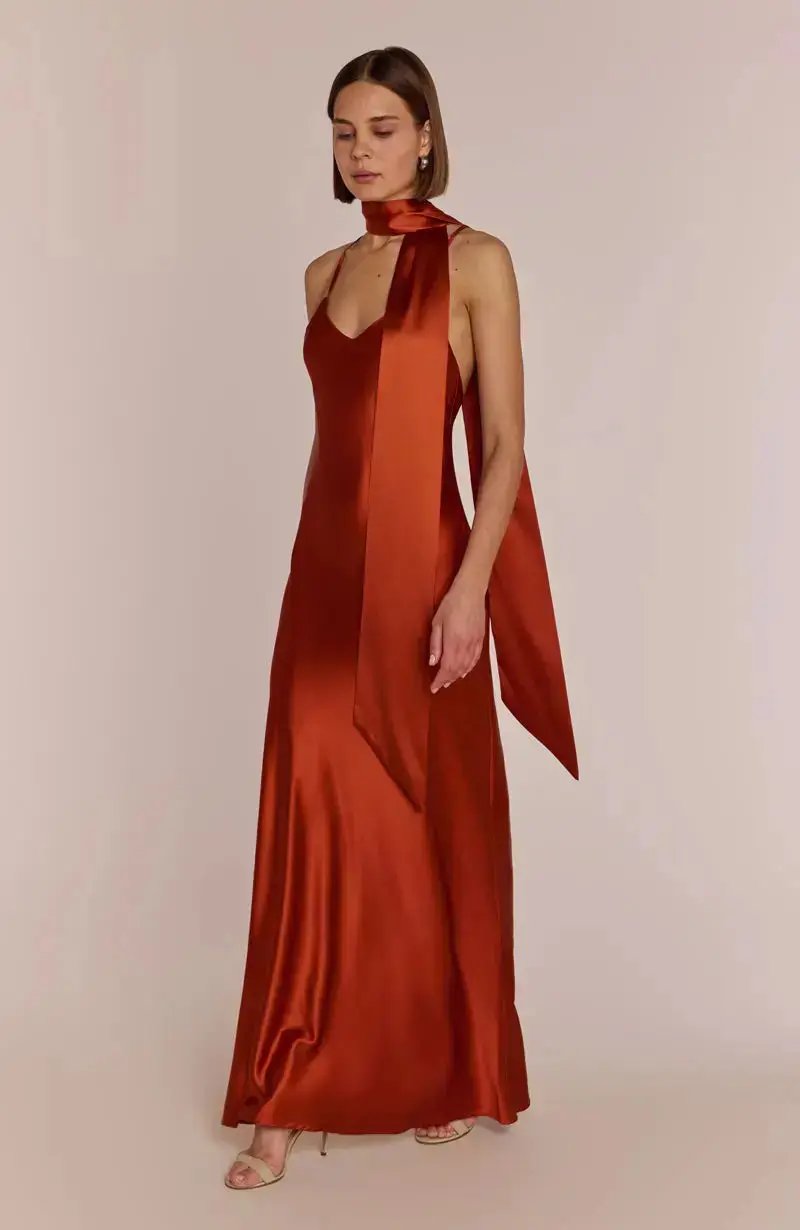 Woman wearing a burnt orange halter neck bridesmaid dress against a plain background