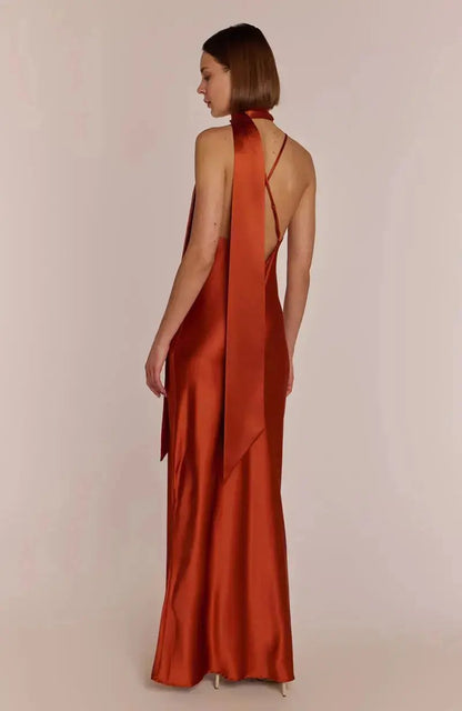 Bridesmaid wearing a rust-colored burnt orange halter neck dress with a draped front on a plain background