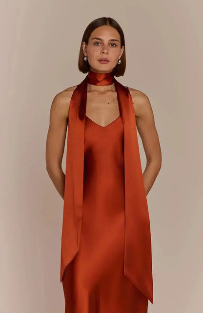 Bridesamid wearing a burnt orange rust-colored dress with a matching scarf against a beige background