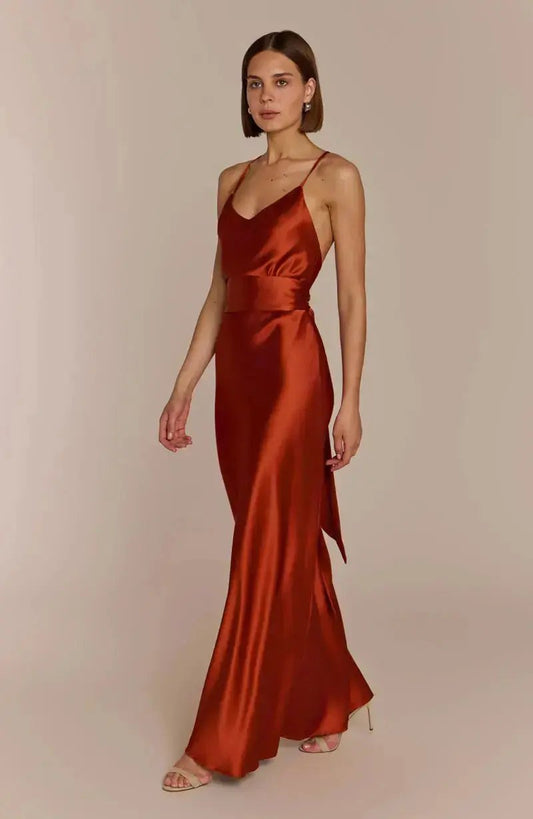 Bridesmaid wearing a rust-colored burnt orange satin dress against a beige background