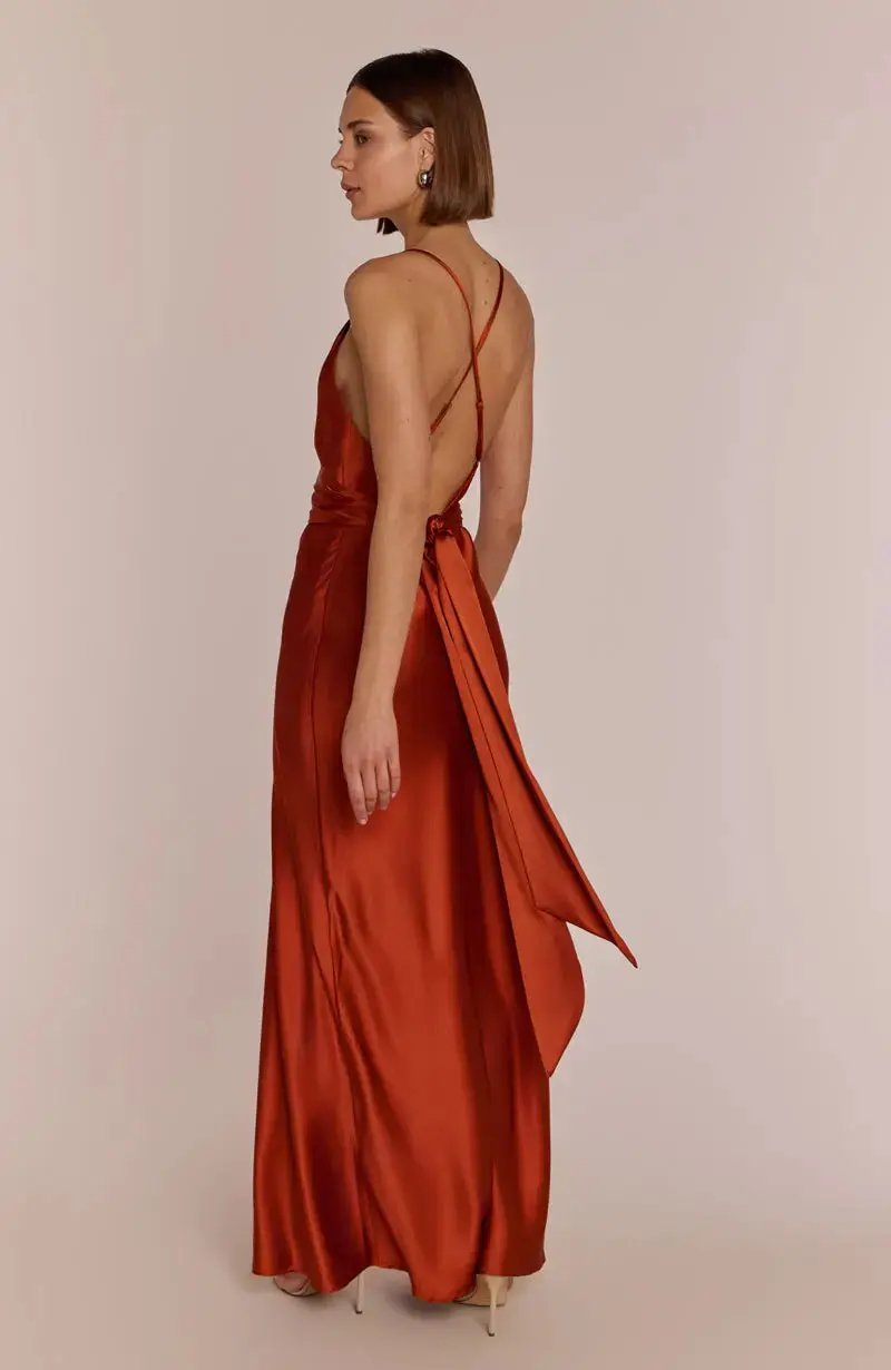 Woman wearing a burnt orange rust-colored satin bridesmaid dress with thin straps on a beige background