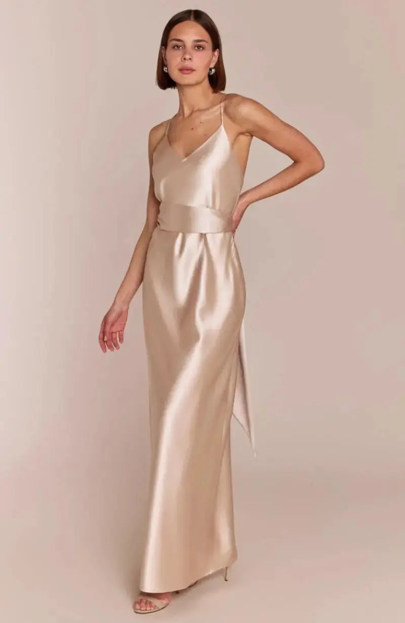 Woman wearing a long, light-colored satin champagne Bridesmaid dress against a plain background
