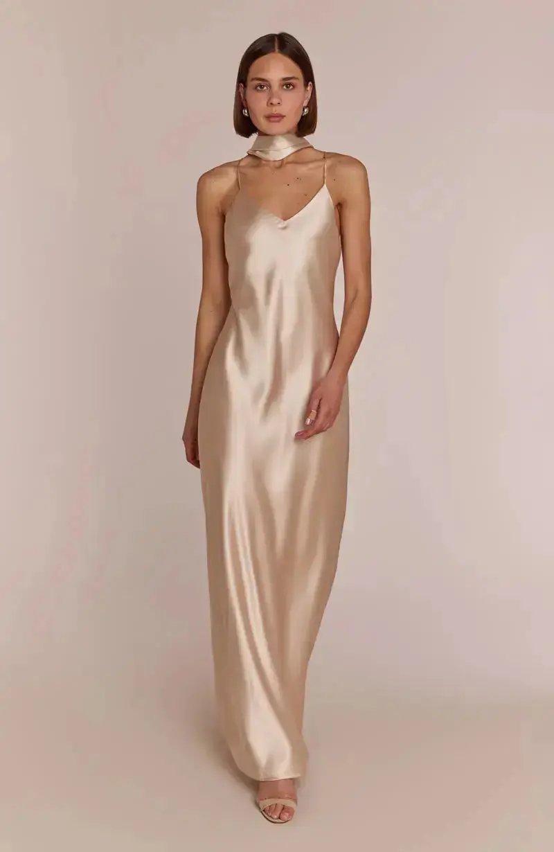 Bridesmaid wearing a champagne slip dress against a plain background