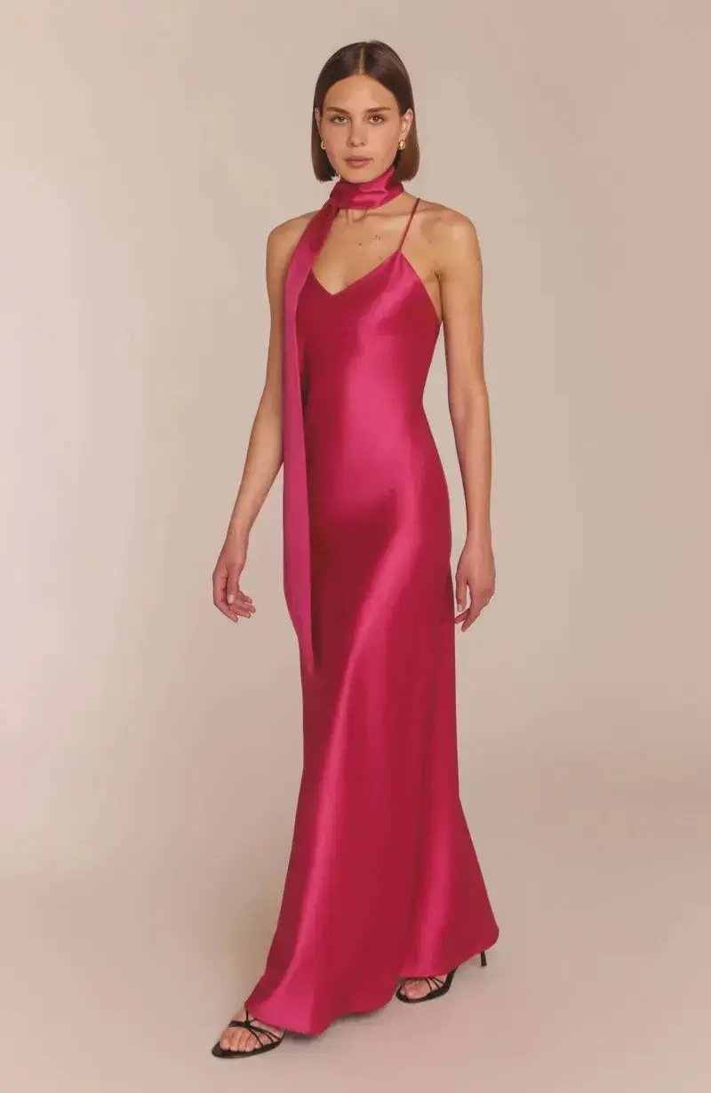 Woman wearing a hot pink fuchsia satin bridesmaid gown against a plain background