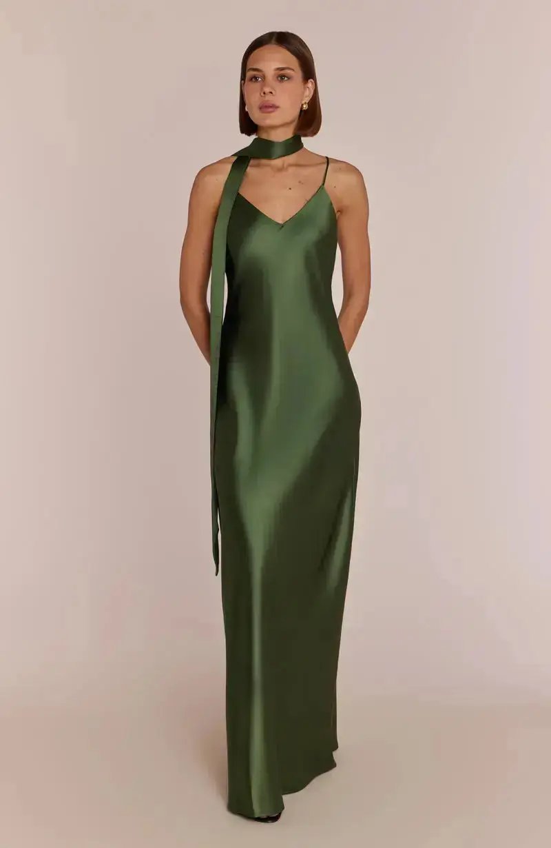 Woman wearing a dark green satin bridesmaid dress against a beige background