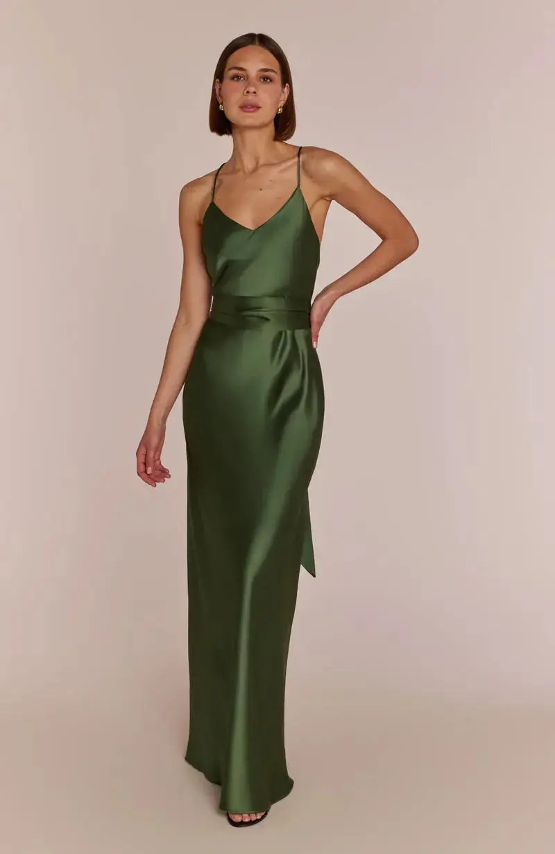 Woman wearing a olive green satin bridesmaid dress against a plain background