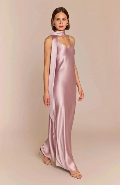 A woman models the Brooklyn bridesmaid Dress in Rose Pink Satin, featuring thin straps and a matching long scarf draped around her neck. Her shoulder-length brown hair stands out against a plain beige background.
