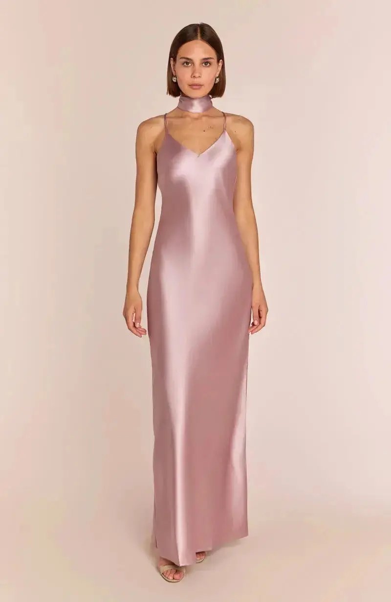 A woman wearing the Brooklyn Dress in Rose Pink Satin, a long sleeveless gown with a choker neckline, stands against a plain light background.