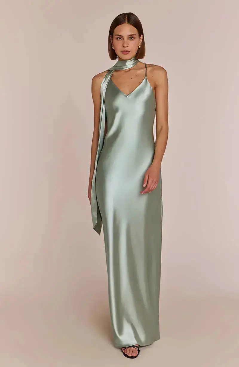 bridesmaid wearing a long, light sage green satin dress against a plain background