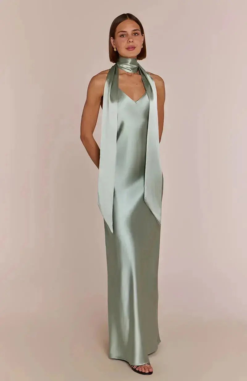 Woman wearing a light sage green satin bridesmaid dress with a long scarf on a beige background