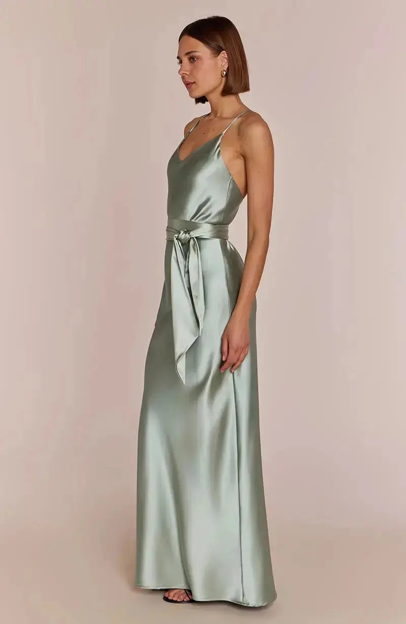 Woman wearing a light sage green satin bridesmaid dress against a plain background