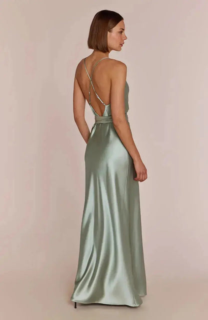 Woman wearing a long, light sage green satin bridesmaid dress with thin straps on a beige background