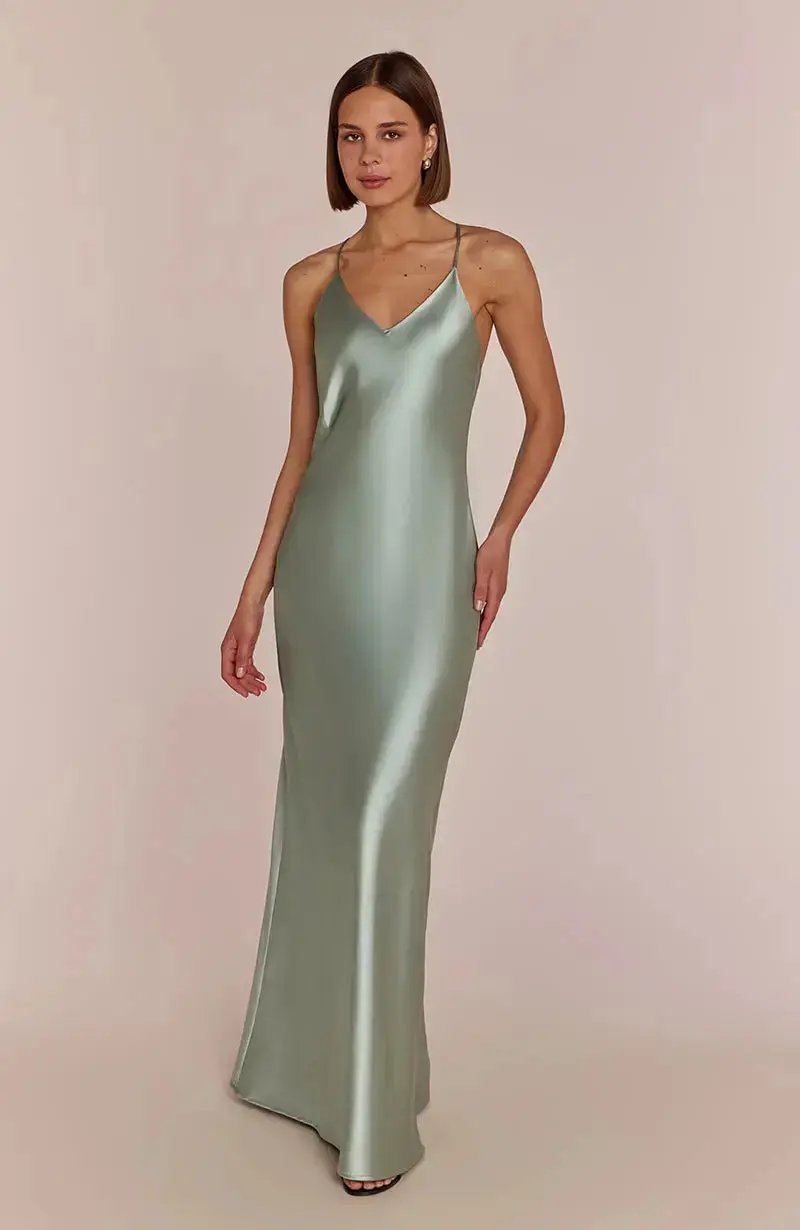Woman wearing a light sage green satin slip bridesmaid dress against a plain background