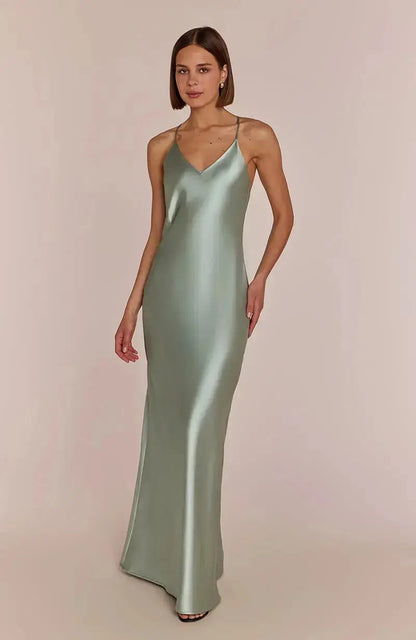 Woman wearing a light sage green satin slip bridesmaid dress against a plain background