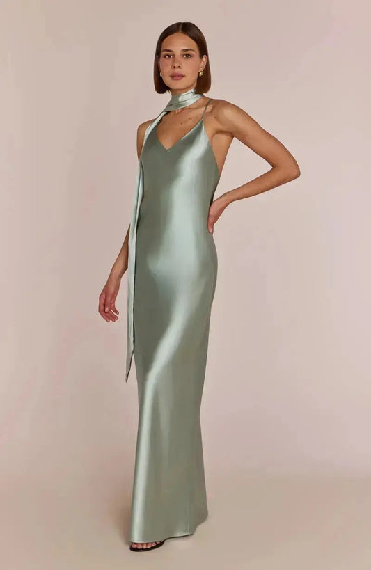 Woman wearing a sage green satin bridesmaid gown with a high neckline on a beige background