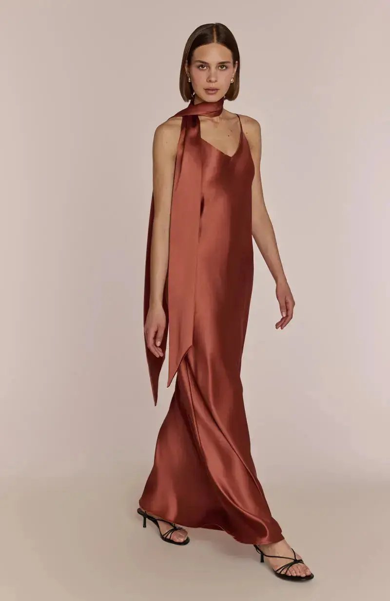 Woman wearing a satin halter neck terracotta brown bridesmaid dress on a beige background