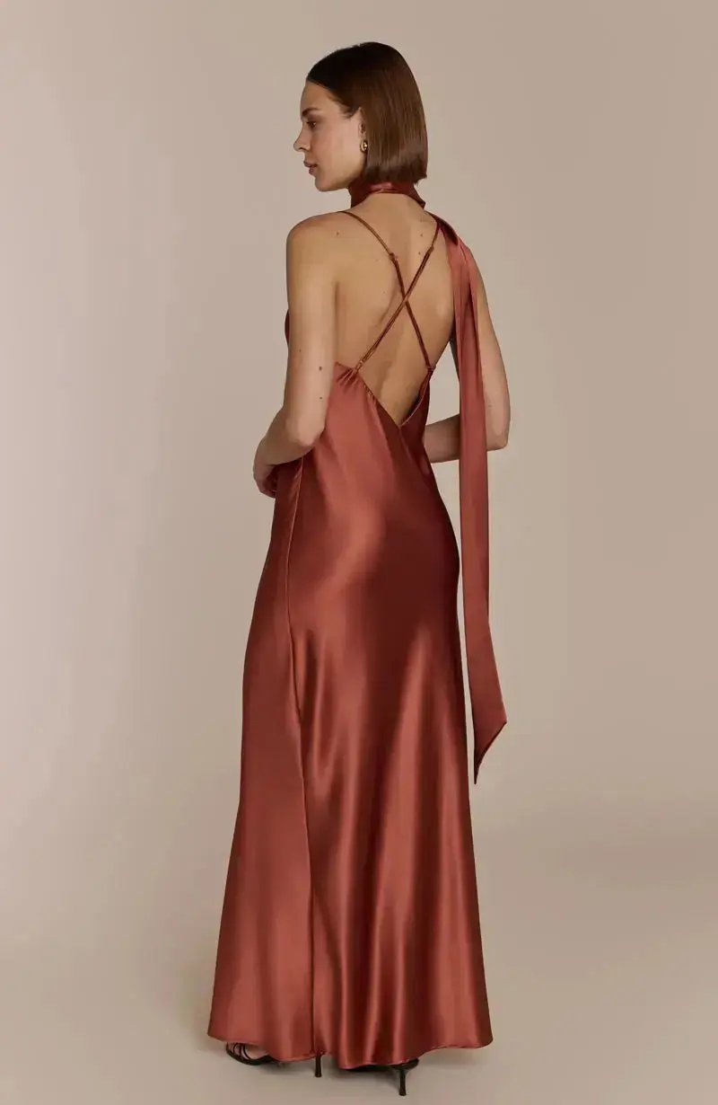 Woman wearing a satin terracotta brown bridesmaid dress with a backless design on a beige background