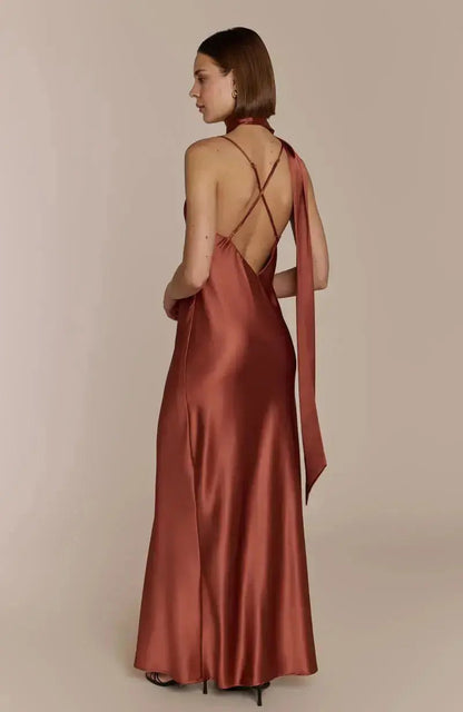 Woman wearing a satin terracotta brown bridesmaid dress with a backless design on a beige background