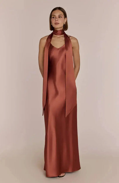 Woman wearing a satin terracotta brown bridesmaid dress with a long scarf on a beige background