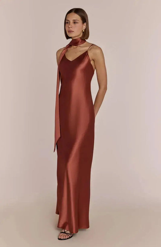 Woman wearing a rust-colored satin terracotta brown bridesmaid dress against a plain background