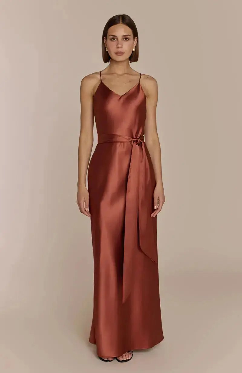 Woman wearing a satin terracotta brown bridesmaid gown against a beige background