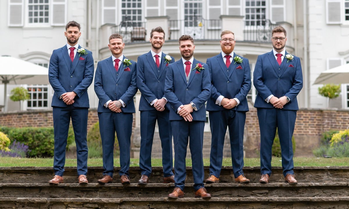 Six groomsmen in blue tweed suits and claret ties standing outside a grand building.