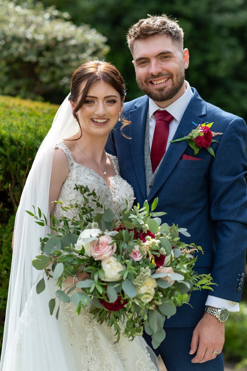 A smiling bride and groom, the bride holding a large bouquet of pink and white flowers.