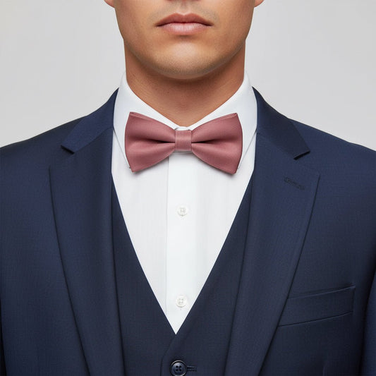 Man wearing a navy suit with a white shirt and pink bow tie on a light gray background