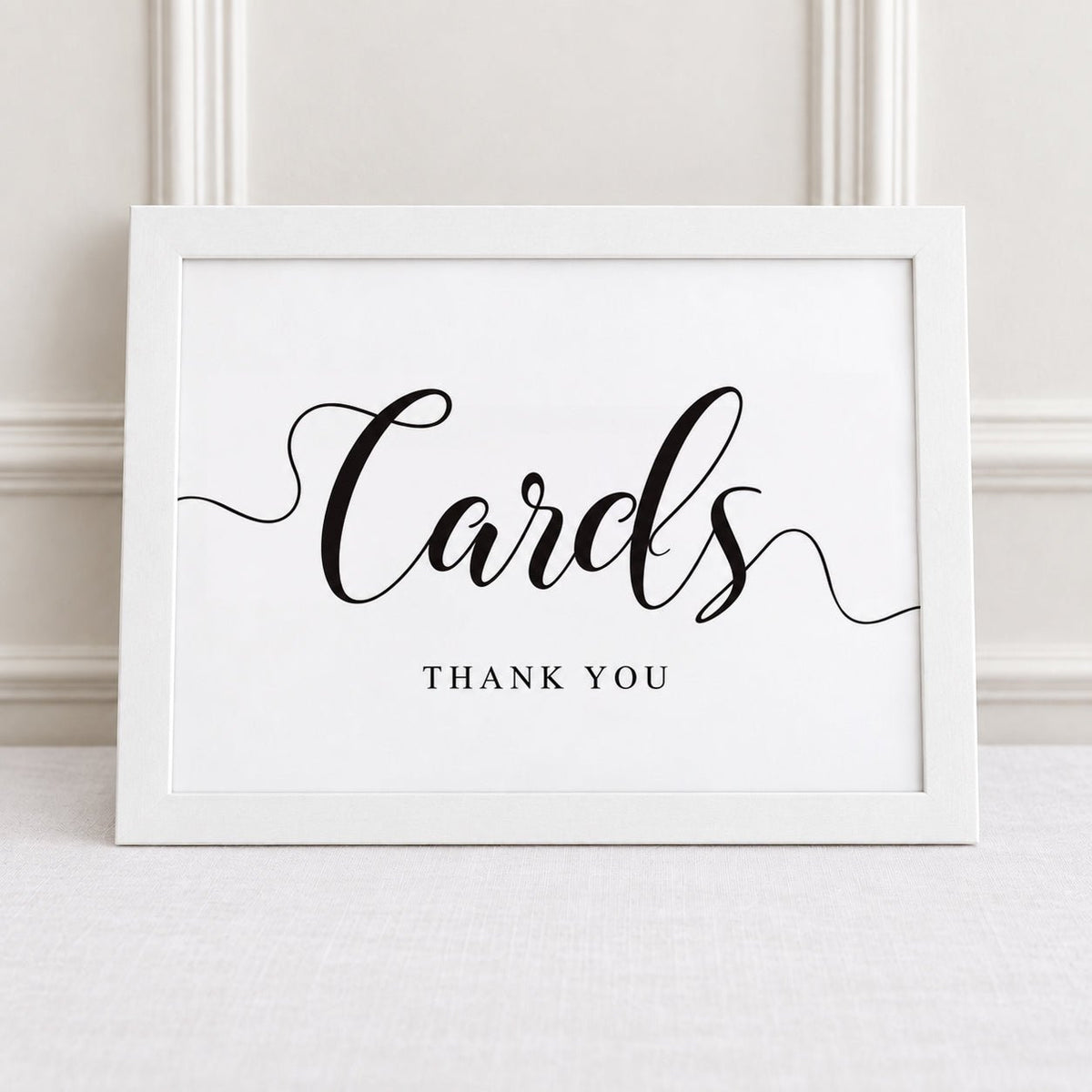 A white framed sign with black script reading 'Cards' and smaller text 'THANK YOU' below, displayed against a light neutral wall.