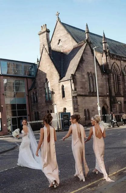 Three bridesmaids in elegant champagne bridesmaid dresses walking behind the bride on a street with a church in the background