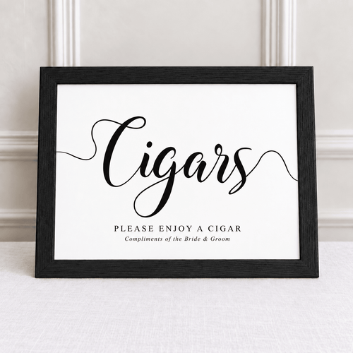 A framed sign with the word "Cigars" in large black script and smaller text reading "Please Enjoy a Cigar" and "Compliments of the Bride & Groom," shown leaning against a light wall on a pale surface.