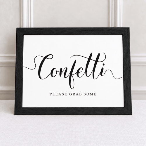 A black-framed sign with the word 'Confetti' in large black script and the phrase 'PLEASE GRAB SOME' underneath, displayed against a light neutral wall and tabletop.