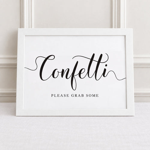 A white framed sign with black script reading 'Confetti' and smaller text 'PLEASE GRAB SOME' below, leaning against a light wall on a pale surface.