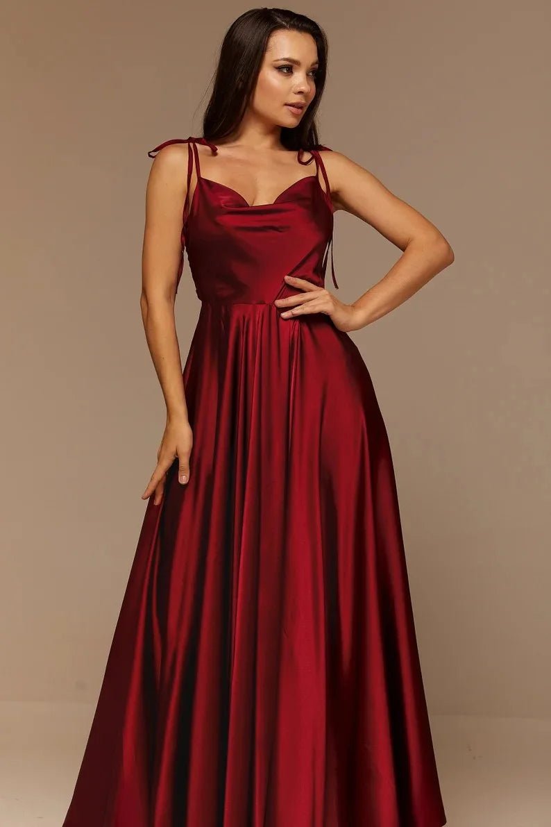 front view of girl wearing burgundy satin side slit backless prom dress with spaghetti straps