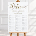 A wedding welcome sign displayed on a wooden easel in a bright interior. The sign is white with elegant gold script reading 'Welcome' and gold personalized text for a wedding of Rebecca & Darren, with a seated guest list printed below.