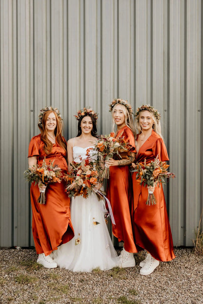 Bride and three bridesmaids in burnt orange bridesmaid dresses standing in front of a metallic wall.