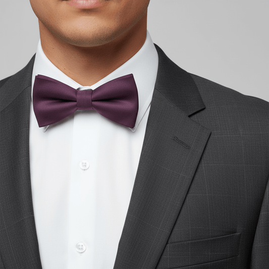 Man wearing a gray suit with a white shirt and purple bow tie on a plain background