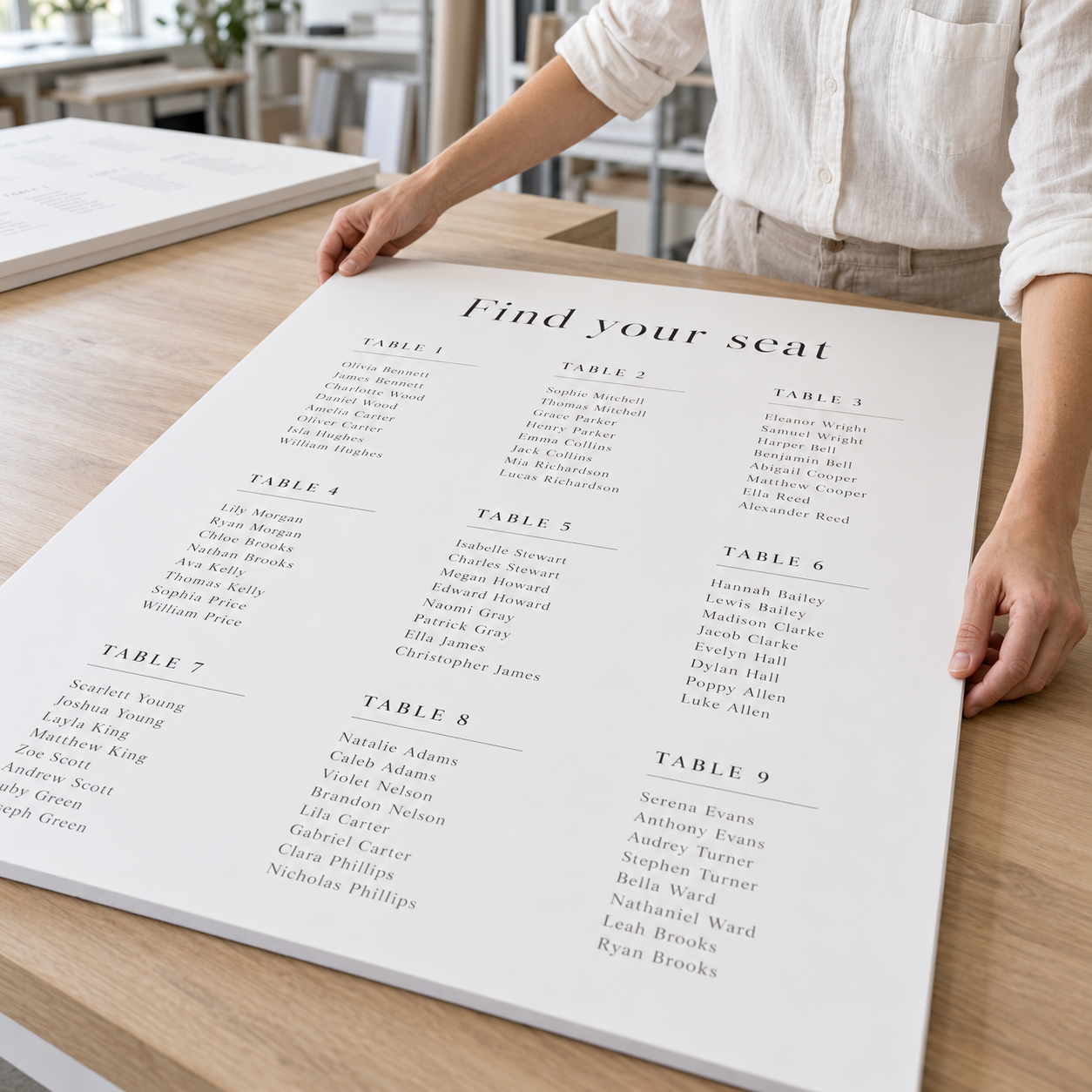 A large printed seating chart template titled 'Find your seat' with tables and names, held on a light wood table by a person wearing a white blouse.