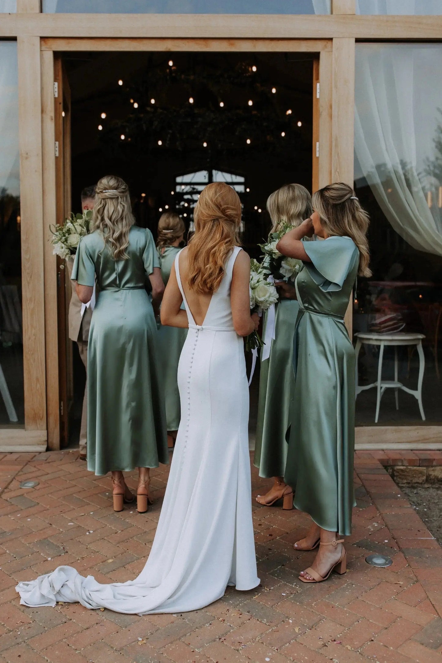Bride in a white dress with bridesmaids in sage green Bridesmaid dresses entering the wedding reception