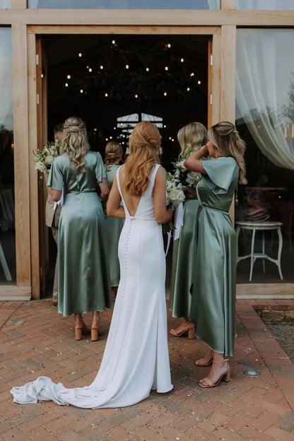 Bride in a white dress with bridesmaids in sage green Bridesmaid dresses entering the wedding reception