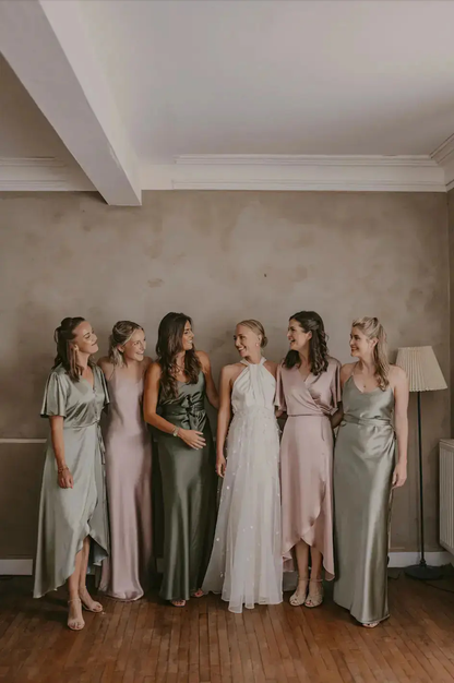 Group of bridesmaids with the bride in formal sage green bridesmaid dresses standing together indoors.