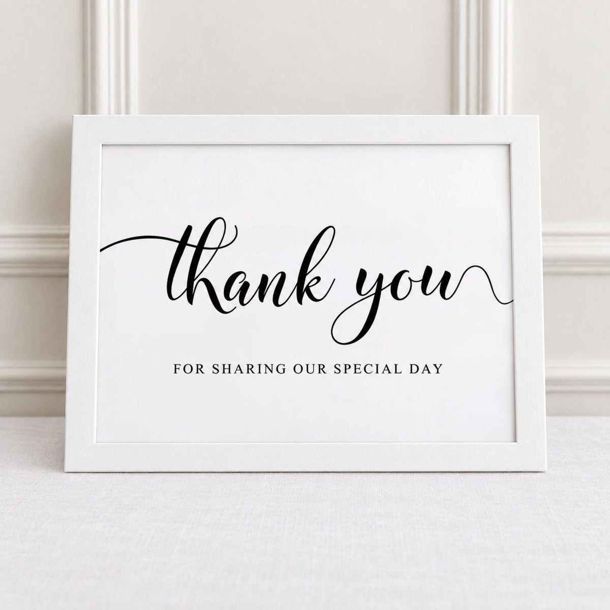 A white framed print with black script reading 'thank you' and smaller text 'FOR SHARING OUR SPECIAL DAY,' displayed against a light paneled wall.