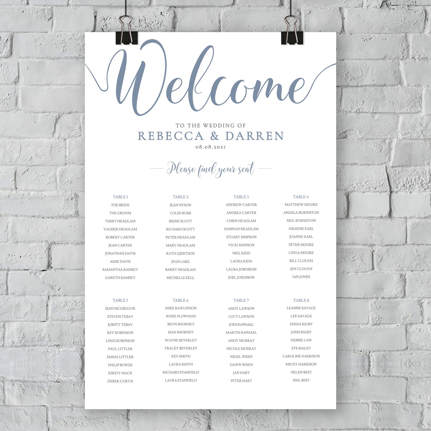 dusty blue seating chart hanging from white brick wall