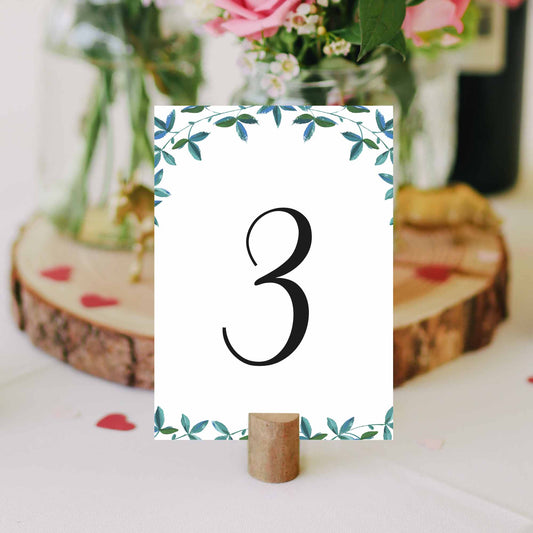 printable table number with green leaves border in a cork stand on a wedding table